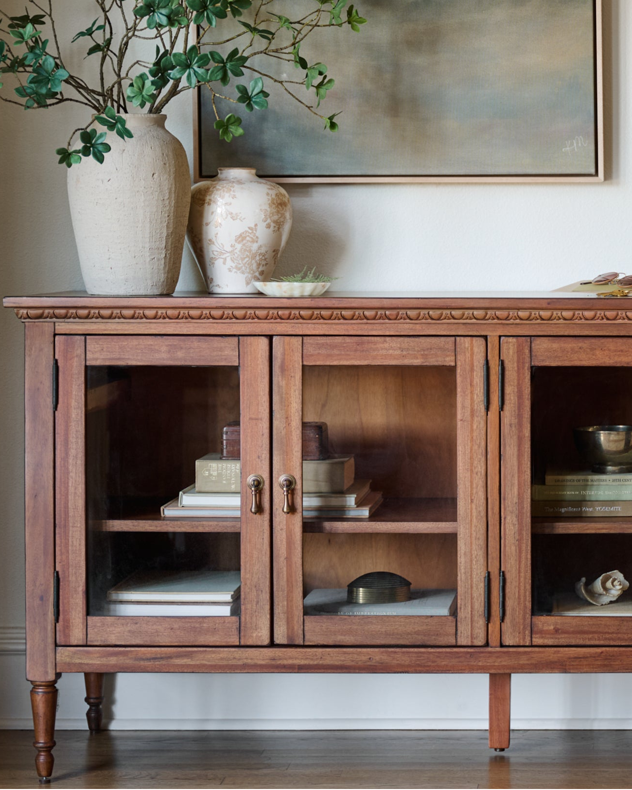 Wooden sideboard with glass doors displaying decorative items, vases, and a plant.