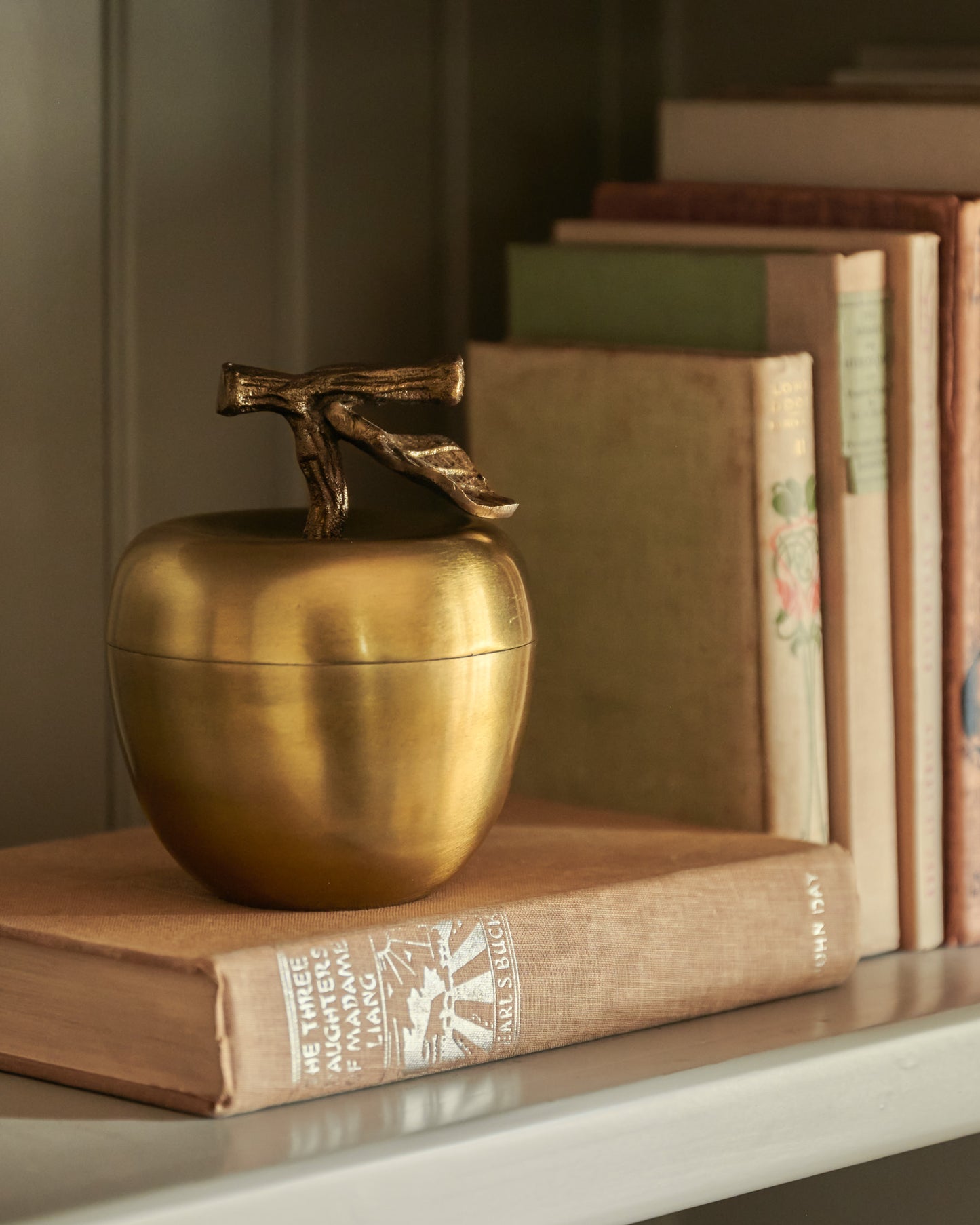 Antique Brass Apple Candle on top of books on shelf