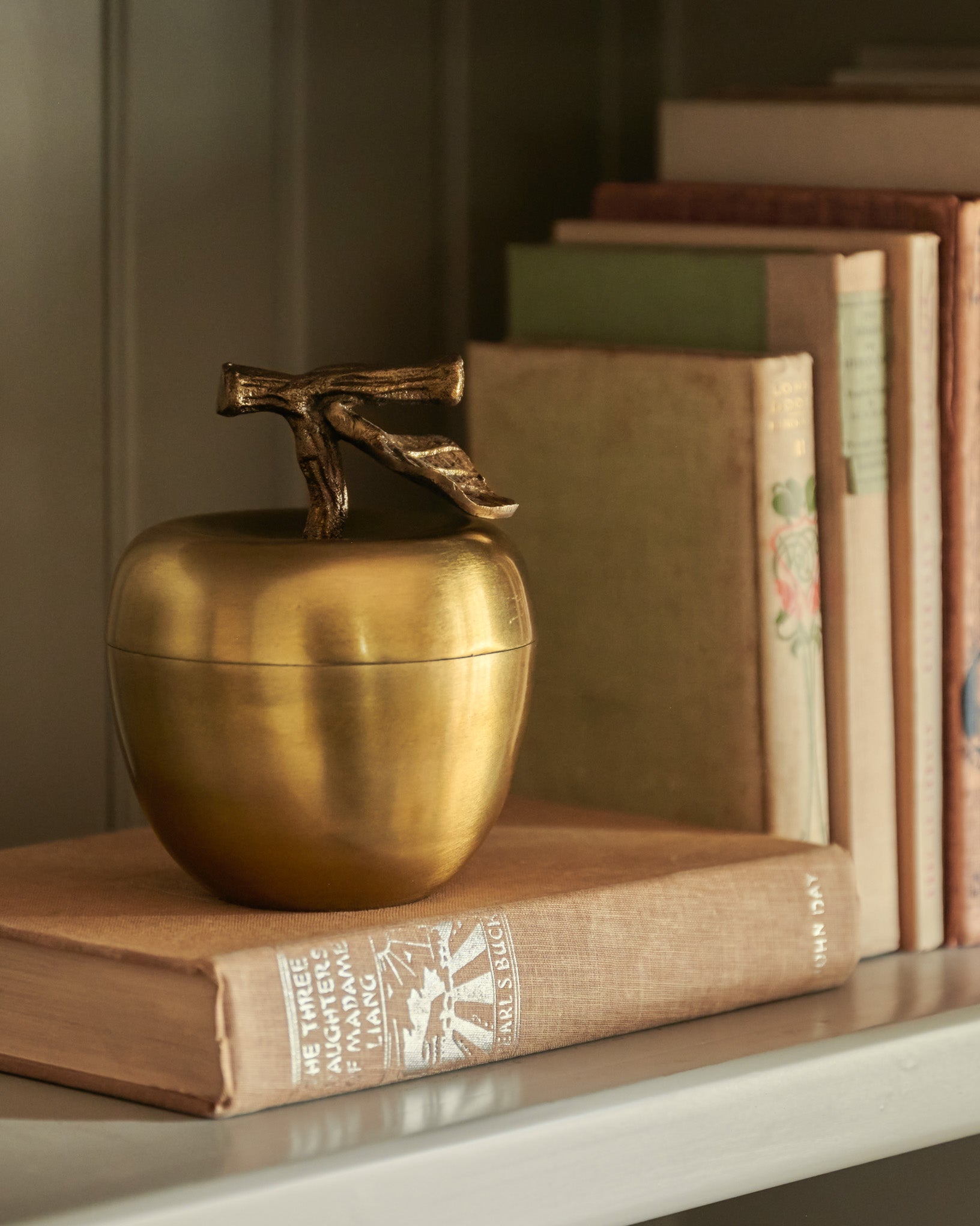 Antique Brass Apple Candle on top of books on shelf