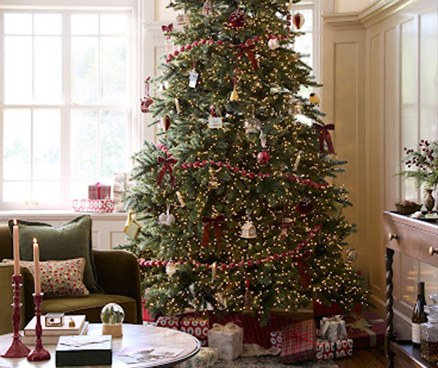 holiday tree decorated with white lights, red garland and ornaments.  below it sits wrapped christmas gifts in a living room.