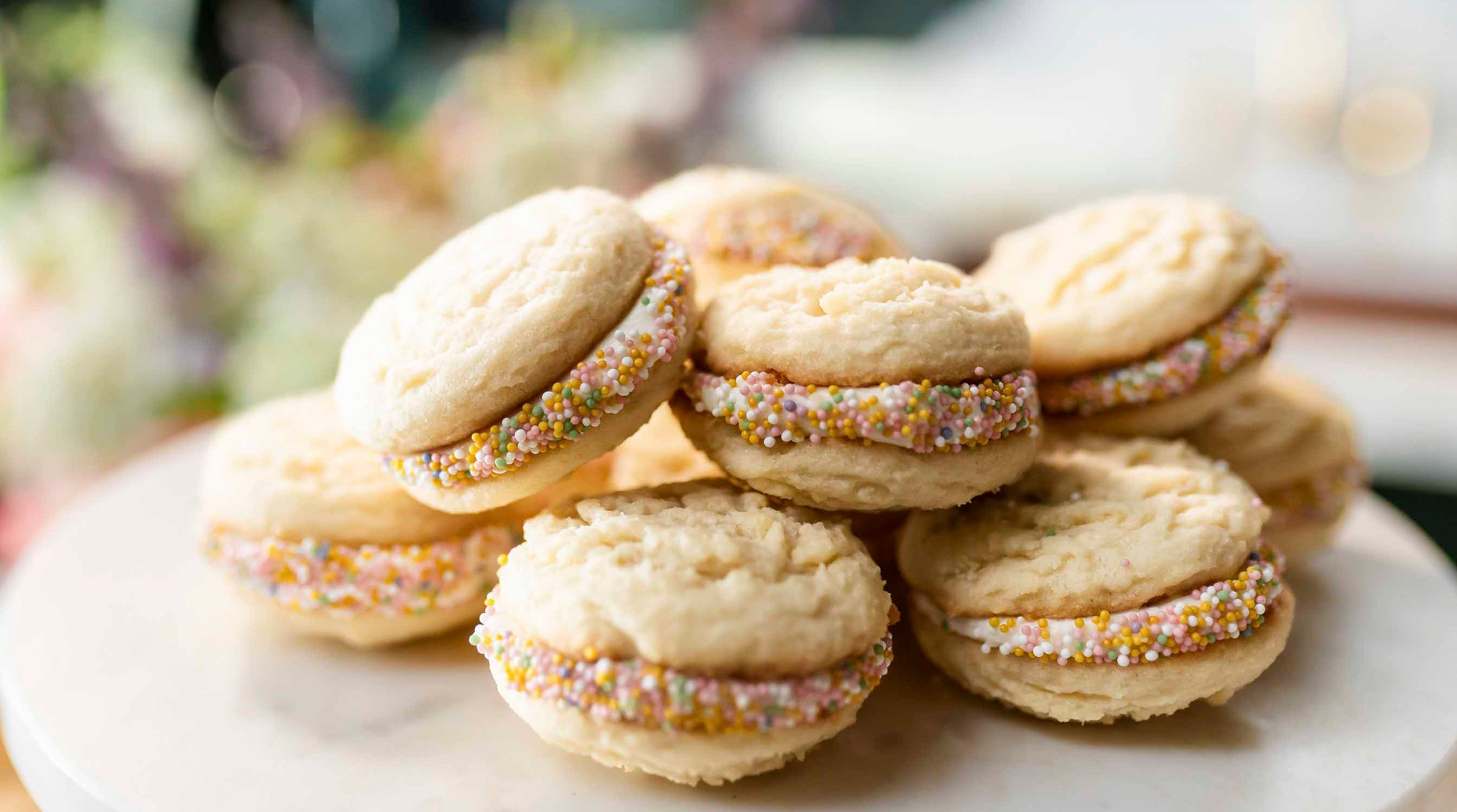Stack of sugar cookie sandwich cookies with sprinkles on a white plate
