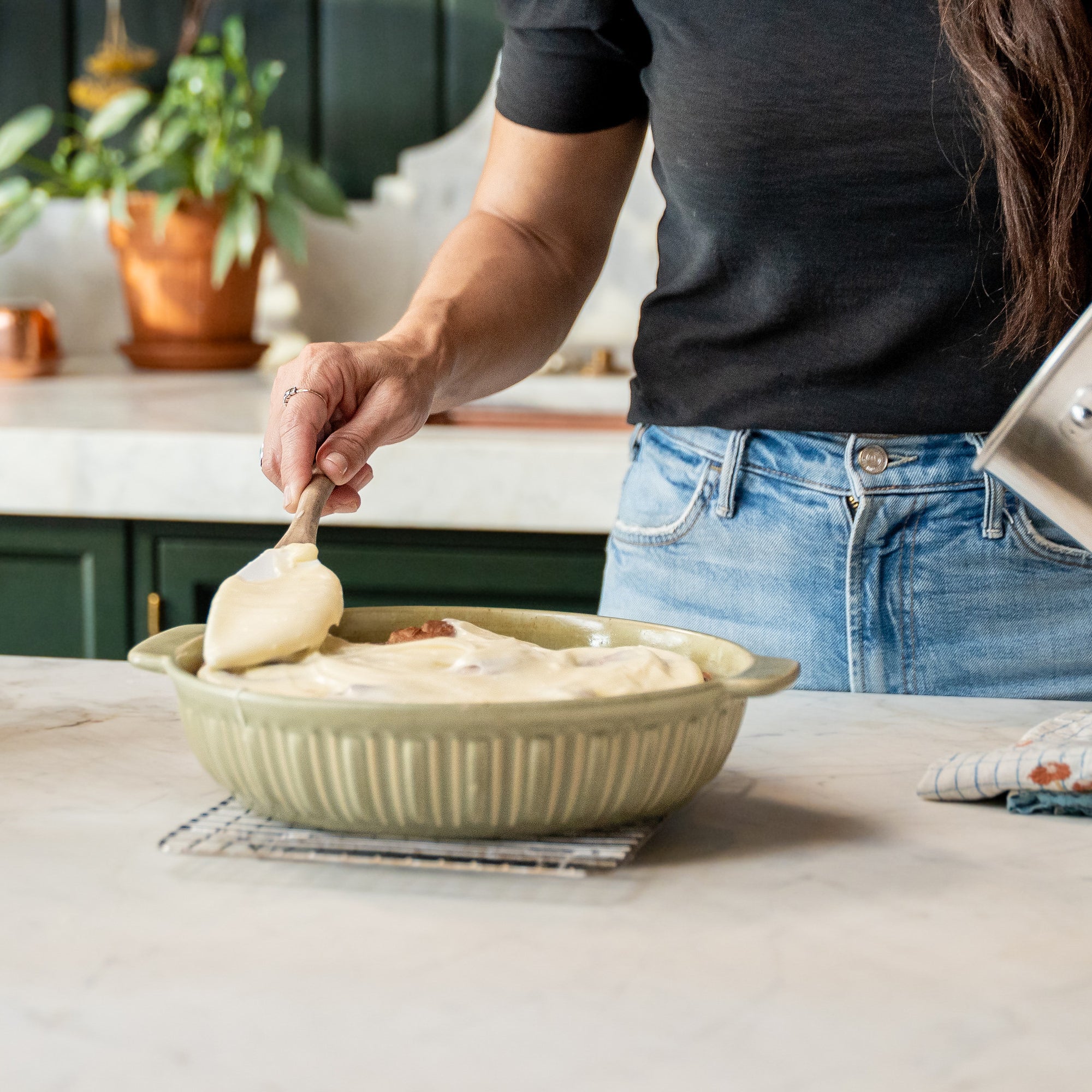 Joanna Gaines preparing cinnamon roles in a kitchen with a baking pan and spatula.