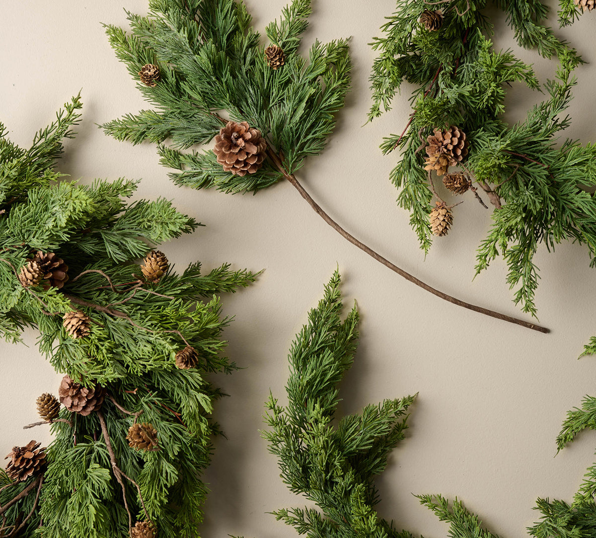 Green pine garland with small pinecones arranged on a light beige background.