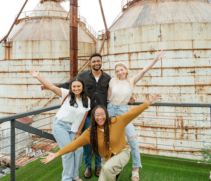 Four people posing in front of large industrial silos with a metal railing.