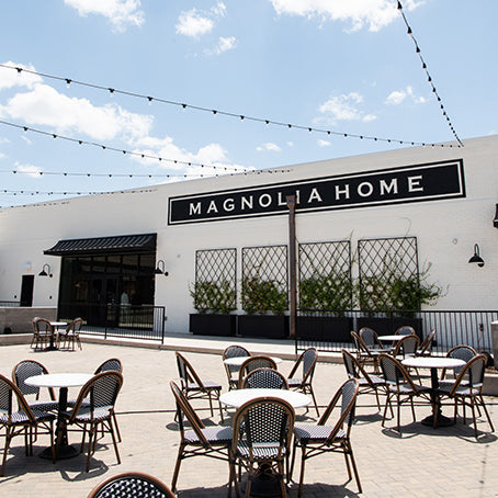 Outdoor seating area with tables and chairs in front of a Magnolia Home building.