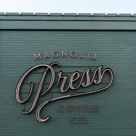 Magnolia Press Coffee Co. sign on a green brick wall