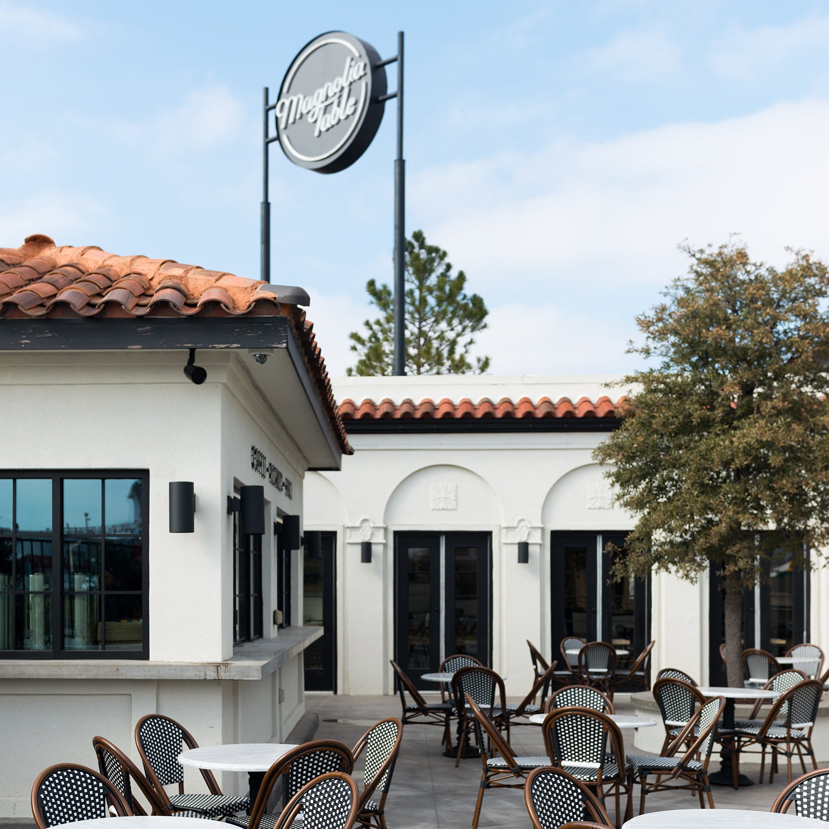 Outdoor seating area at Magnolia Table with tables and chairs outside a building with a sign above.