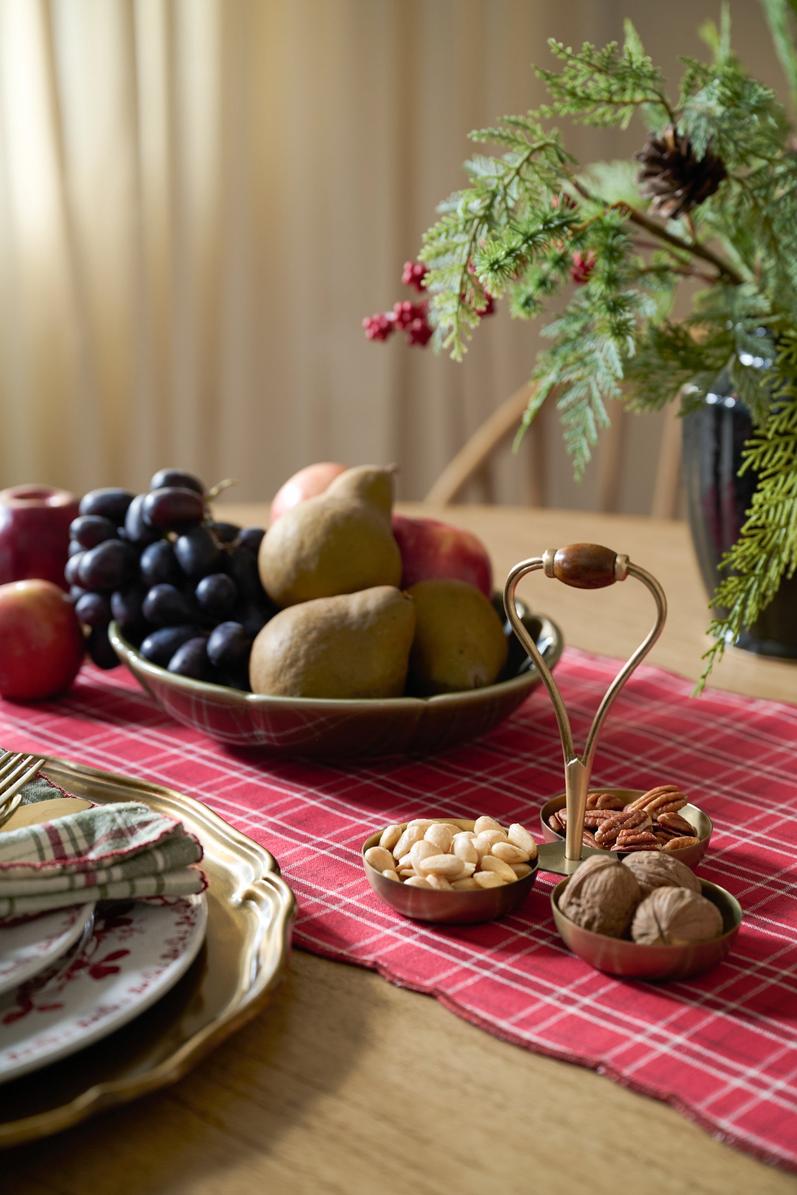 Festive table setting with fruits, nuts, and a plant on a red checkered tablecloth.