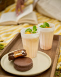 Two cups with a dessert on a tray outdoors, with a person reading a book in the background.