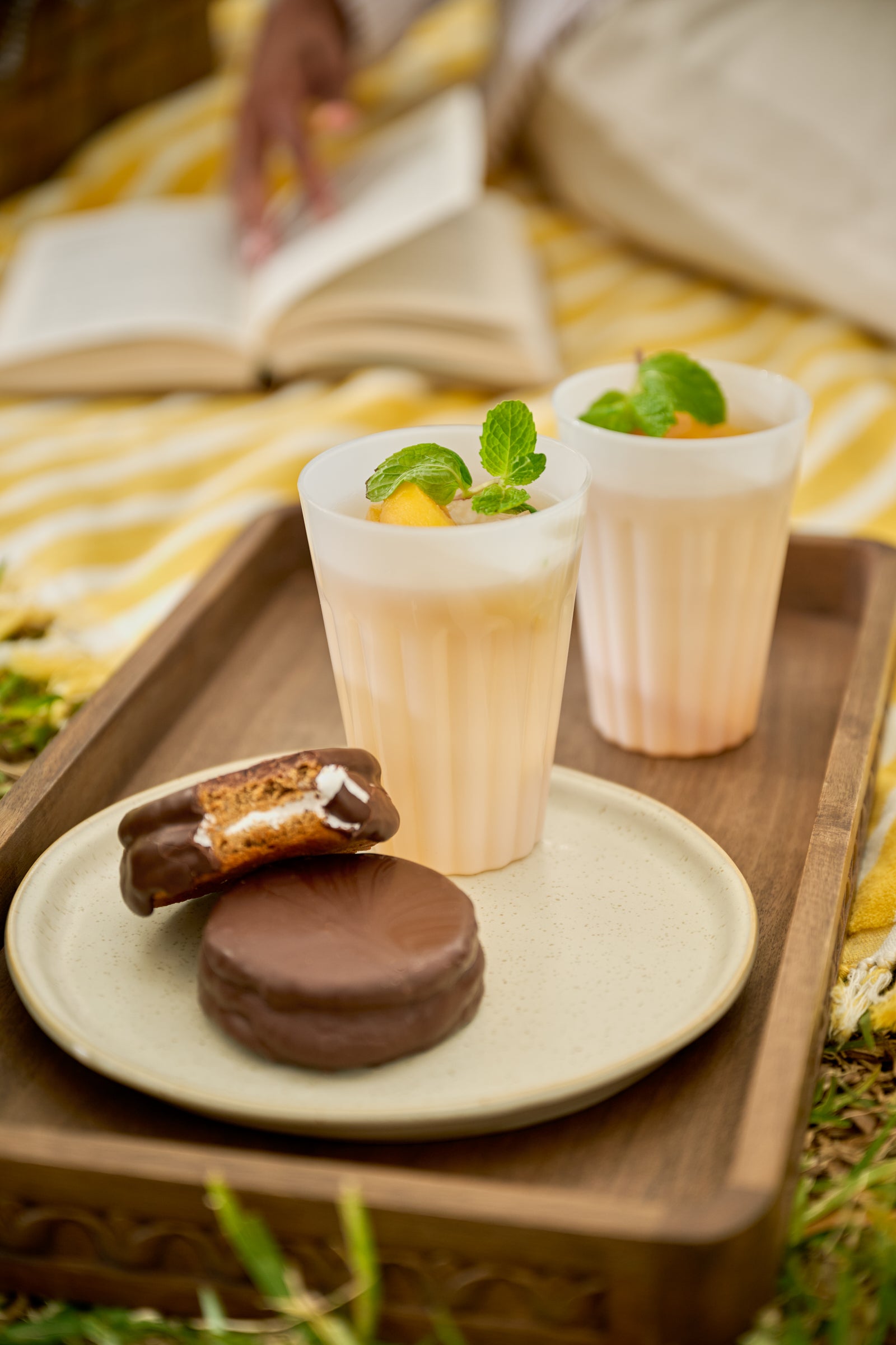 Two cups with a dessert on a tray outdoors, with a person reading a book in the background.