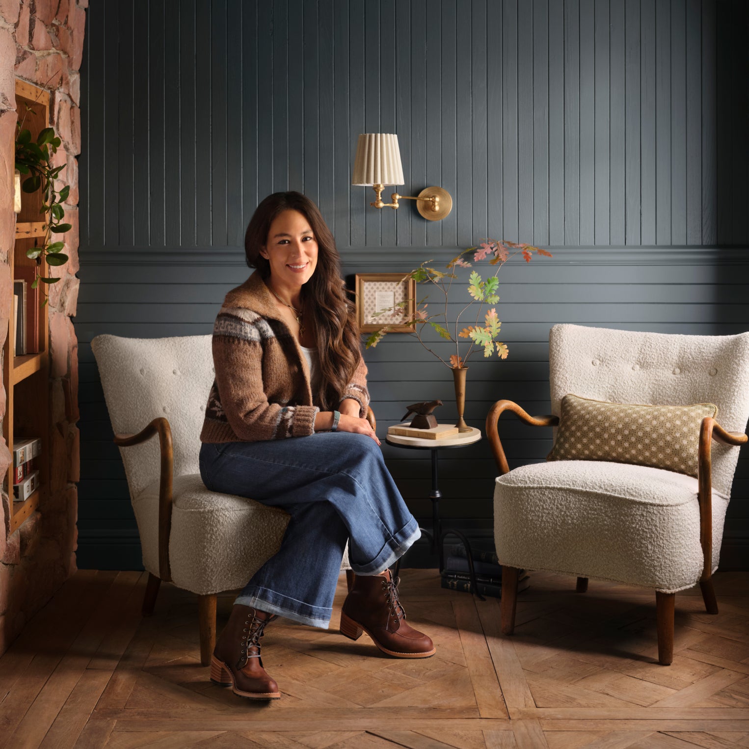 Joanna Gaines sitting on a chair in a cozy room with wooden floors and decorative elements.