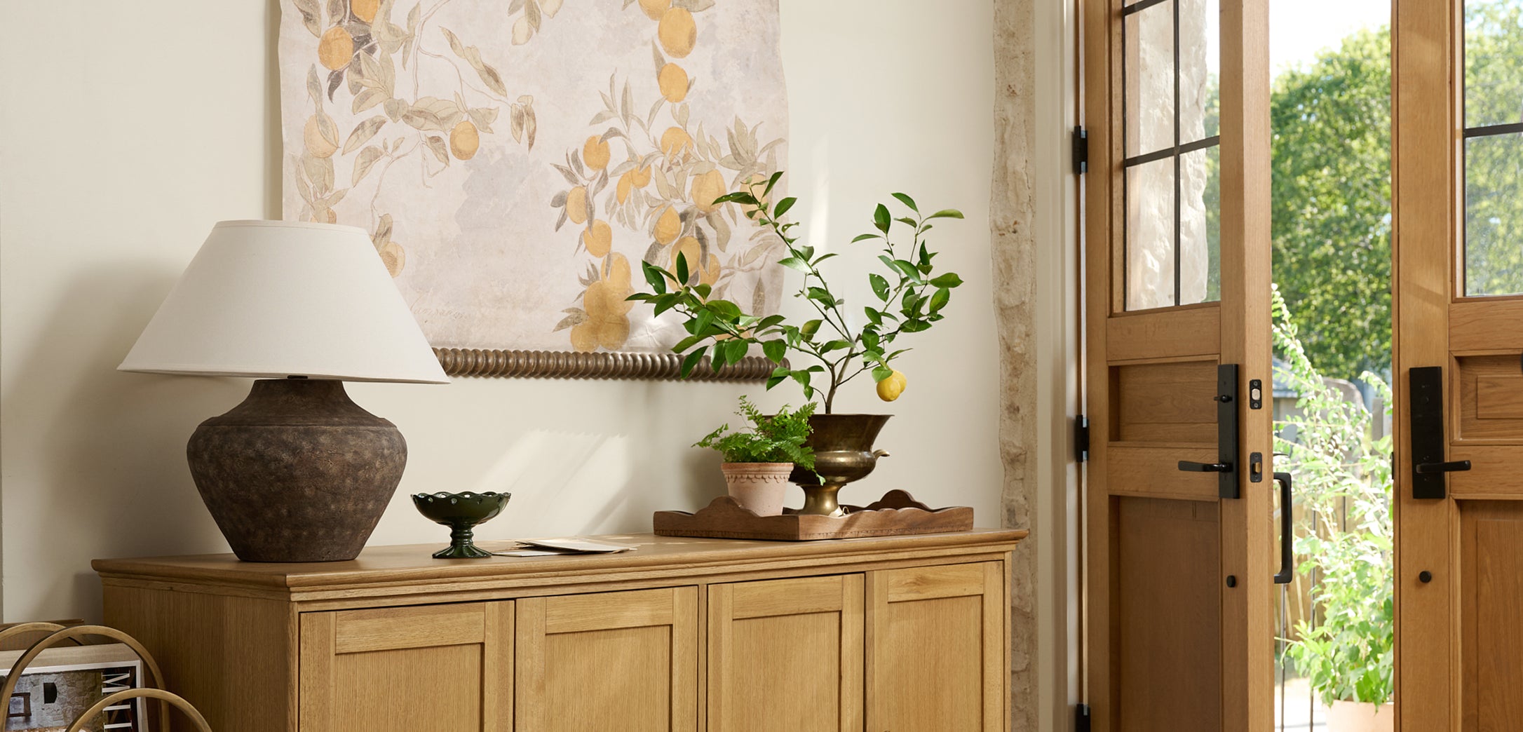 Wooden sideboard with decorative items in a room with a floral painting and open door.