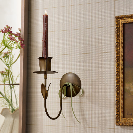 Antique Brass Forged Tulip Wall Sconce with lit taper candle on wall