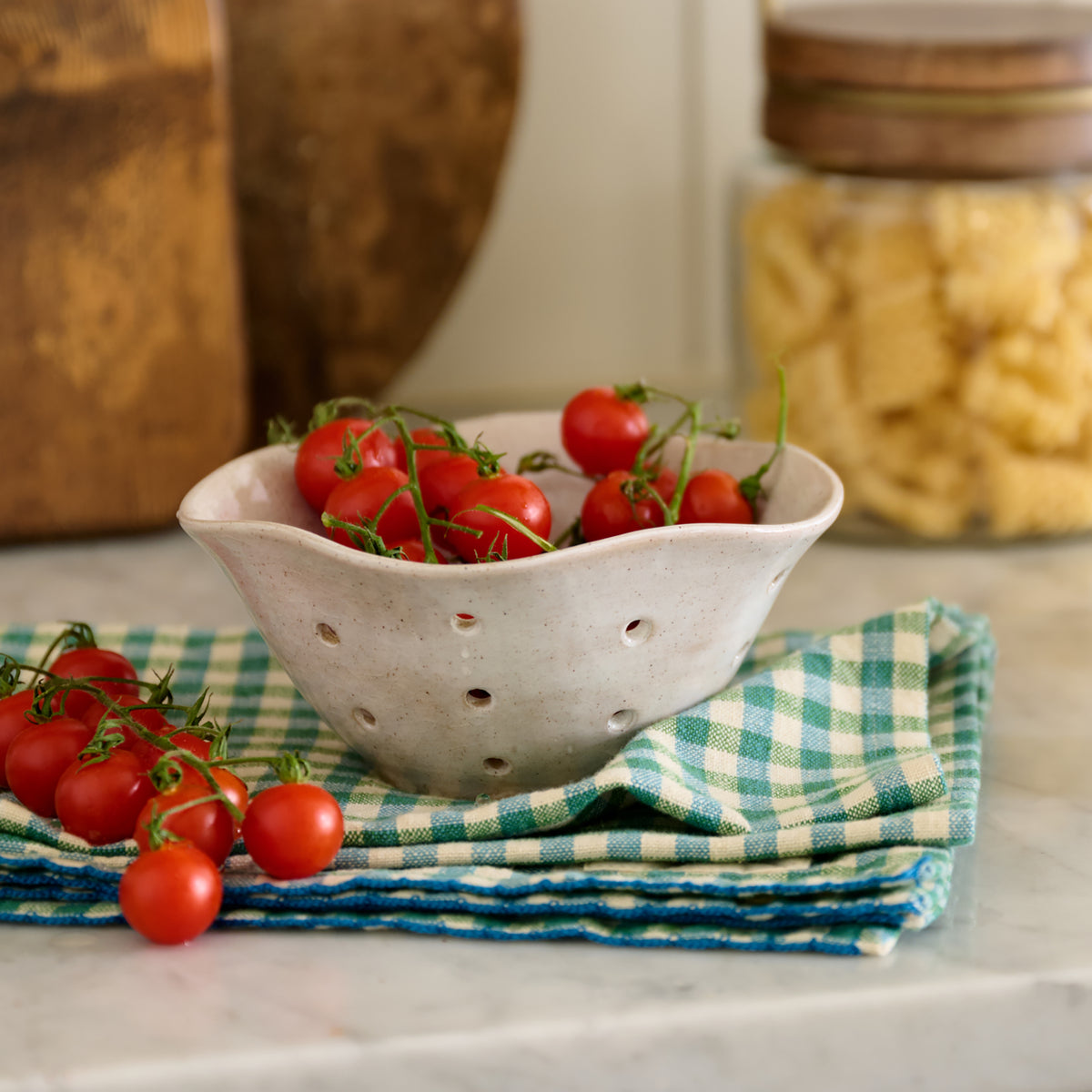 White ceramic colander with cherry tomatoes on a checkered cloth