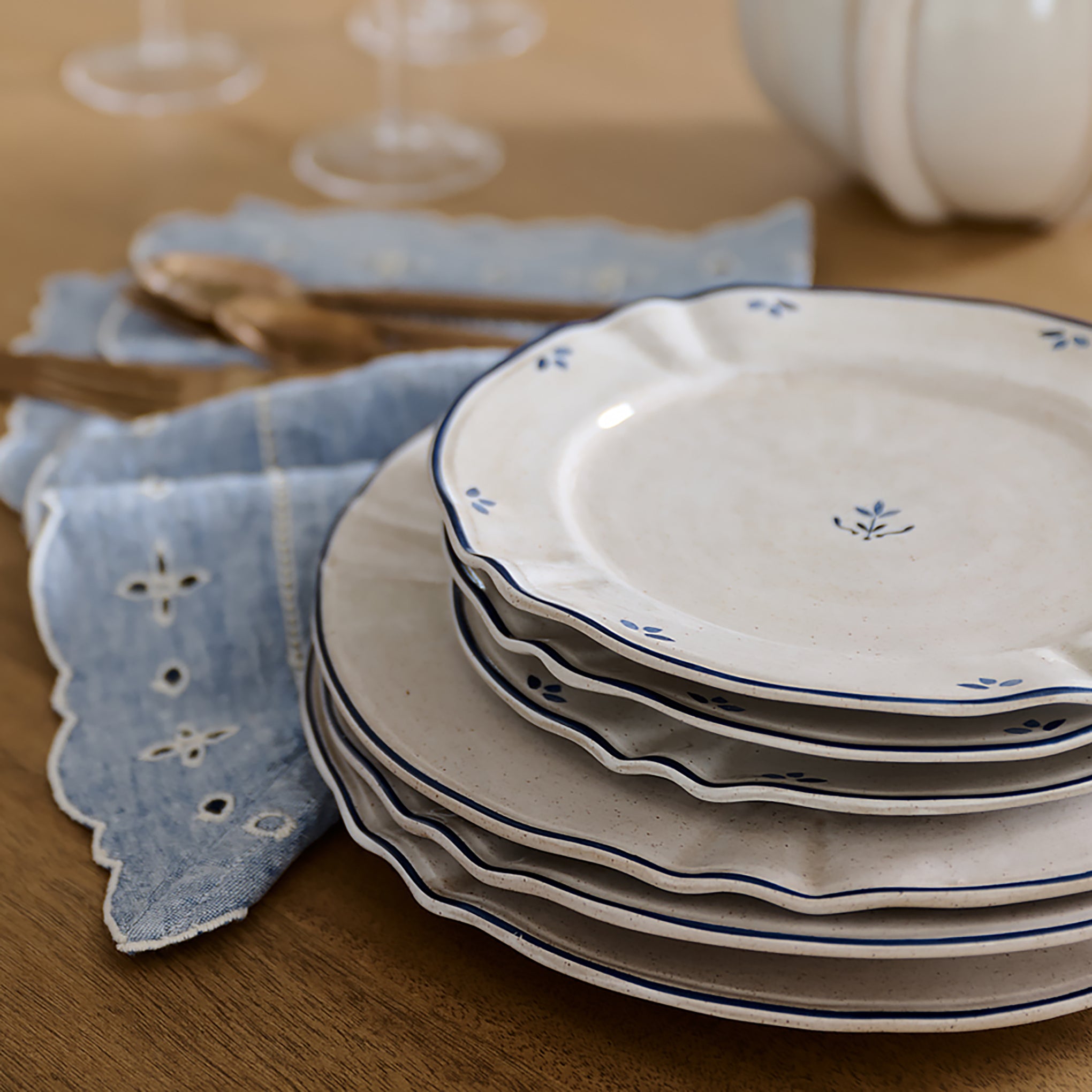 Stack of ceramic plates with blue floral patterns on a wooden table with a blue cloth.