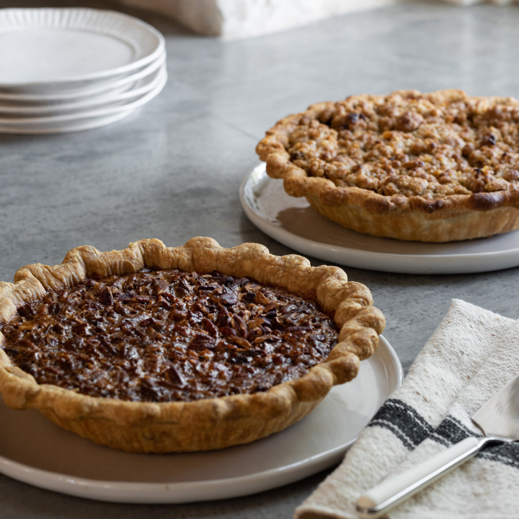 Two pies on plates with a napkin and fork on a gray surface