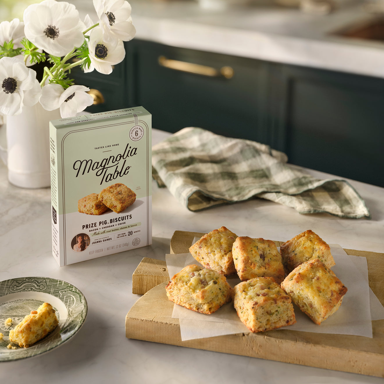 A box of Magnolia Table Frozen Prize Pig Biscuits and a wooden serving board full of baked prize pig biscuits on top of parchment paper.