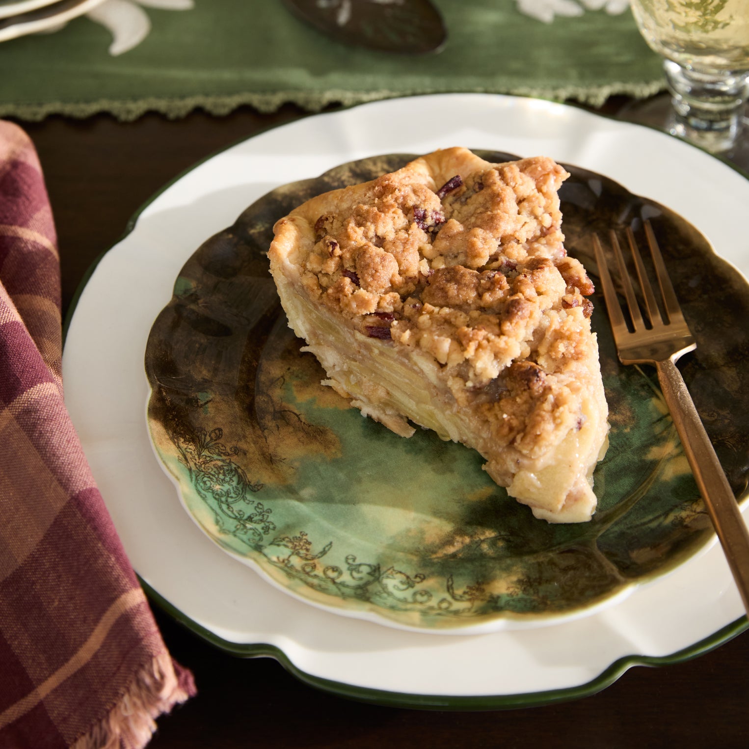 Slice of pie on a decorative plate with a fork, placed on a tablecloth.