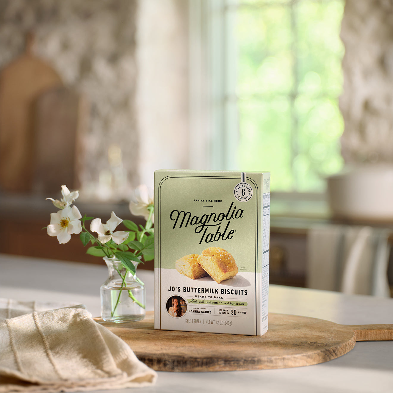 Box of Frozen Magnolia Table Jo's Buttermilk Biscuits on a table with flowers in the background.
