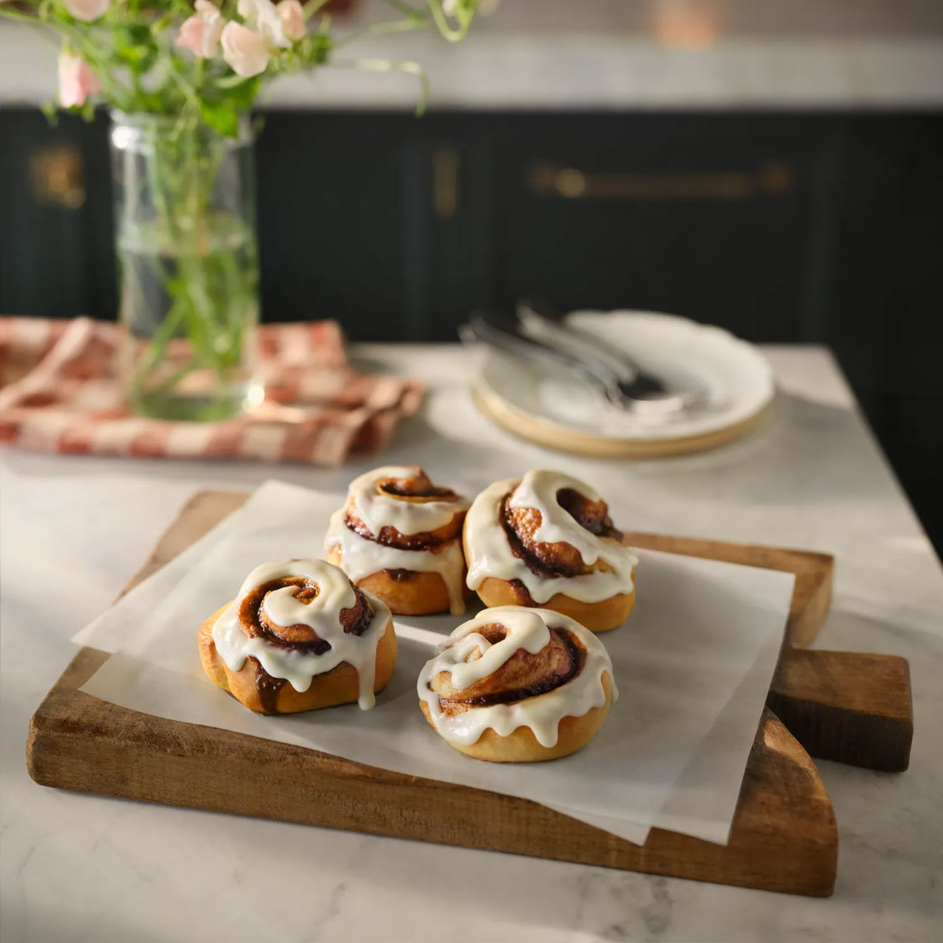 Magnolia Table Classic Cinnamon Rolls with cream cheese icing on a wooden board.