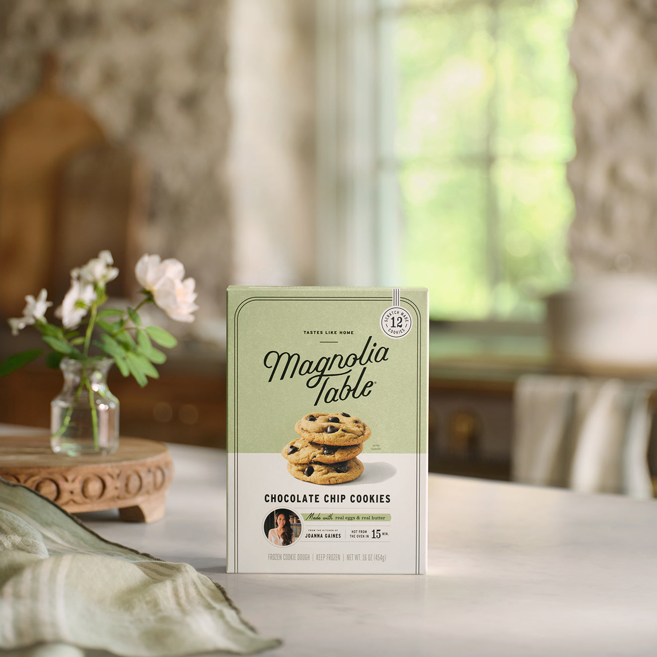 Box of Frozen Magnolia Table Chocolate Chip Cookie Dough on a table with flowers in the background.