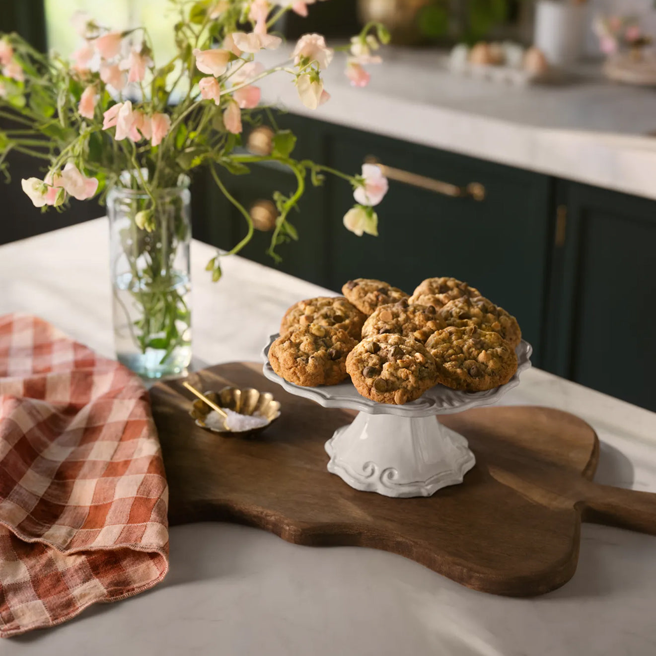 Baked Magnolia Table Silo Cookies on a white cake stand with flowers and a checkered cloth in the background.