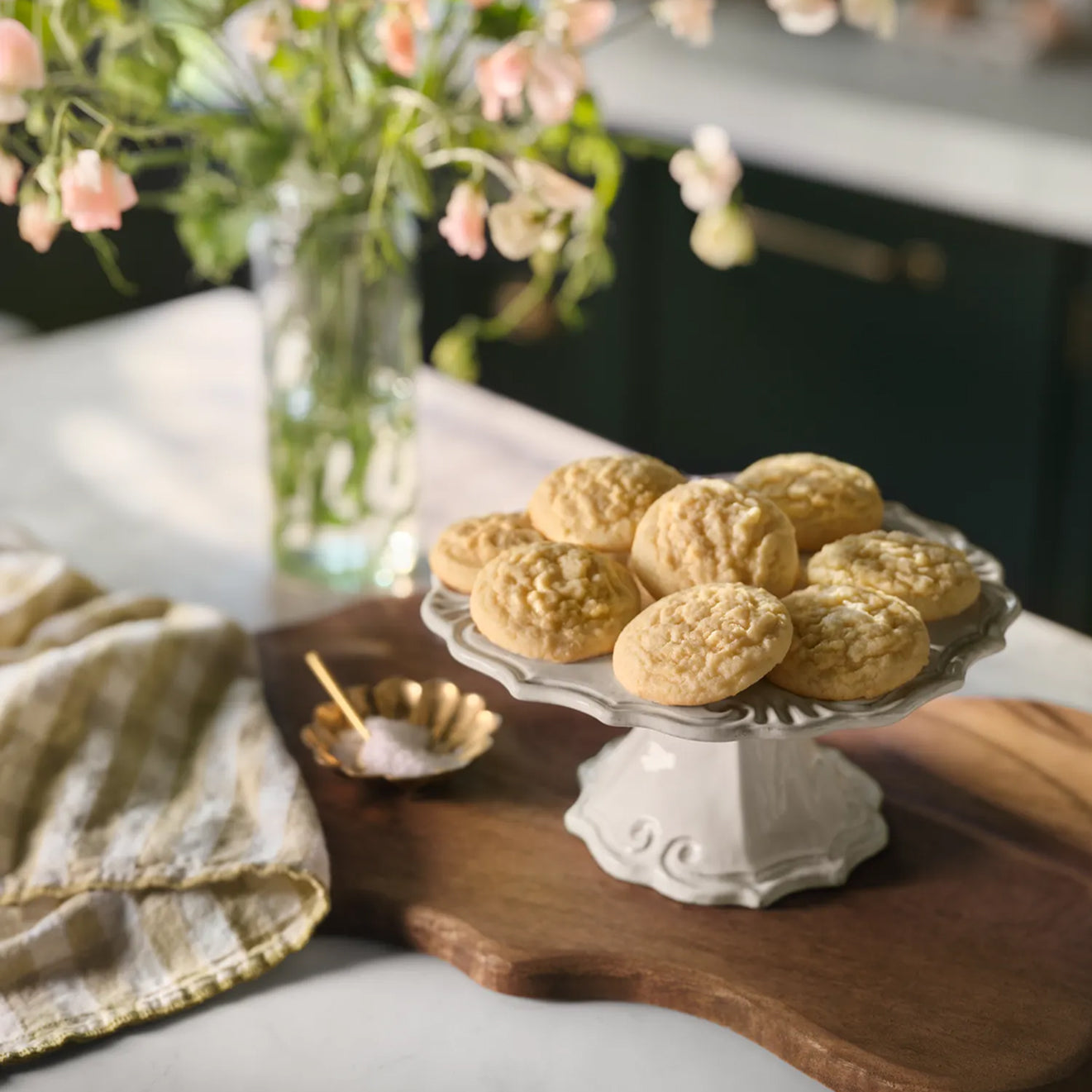 Decorative plate of Magnolia Table Classic Sugar Cookies on a wooden tray with flowers in the background.