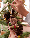 Person decorating a Christmas tree with a cuckoo clock ornament.