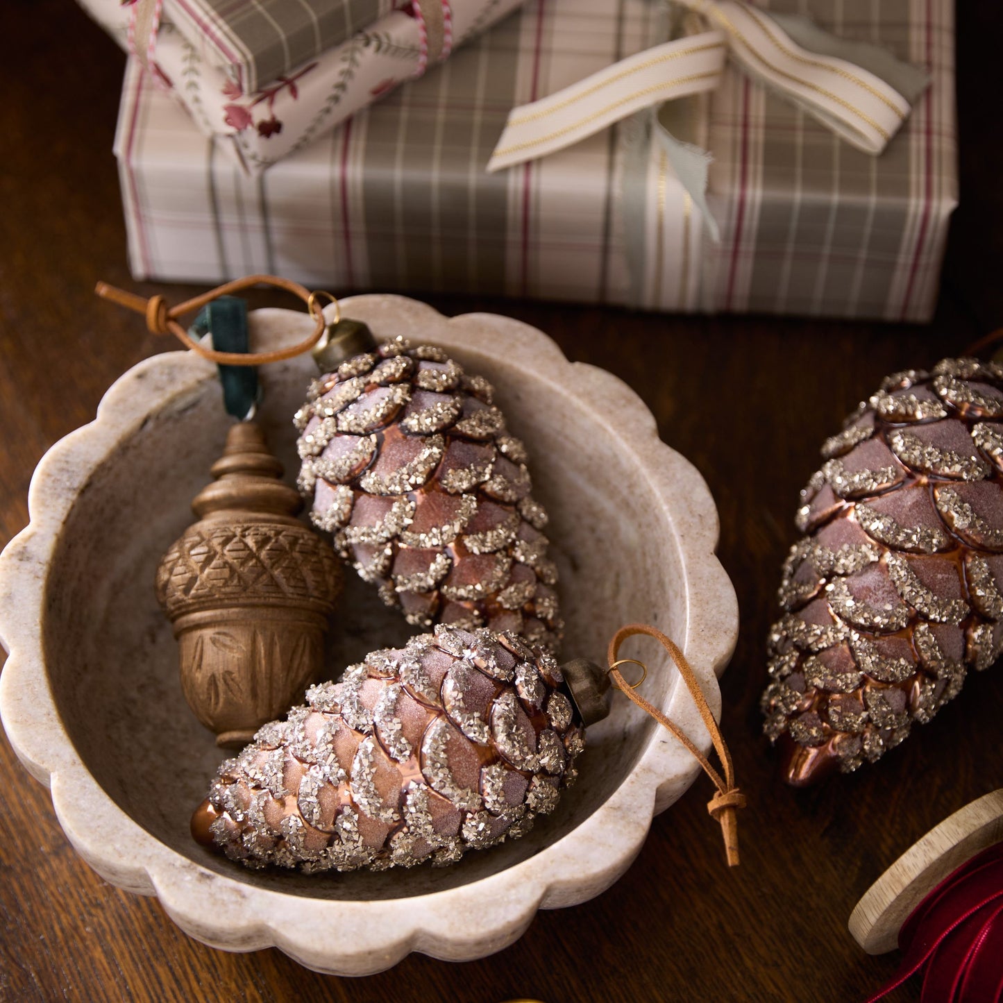 Decorative pinecones with glitter and an acorn in a white dish, with a gift box in the background.