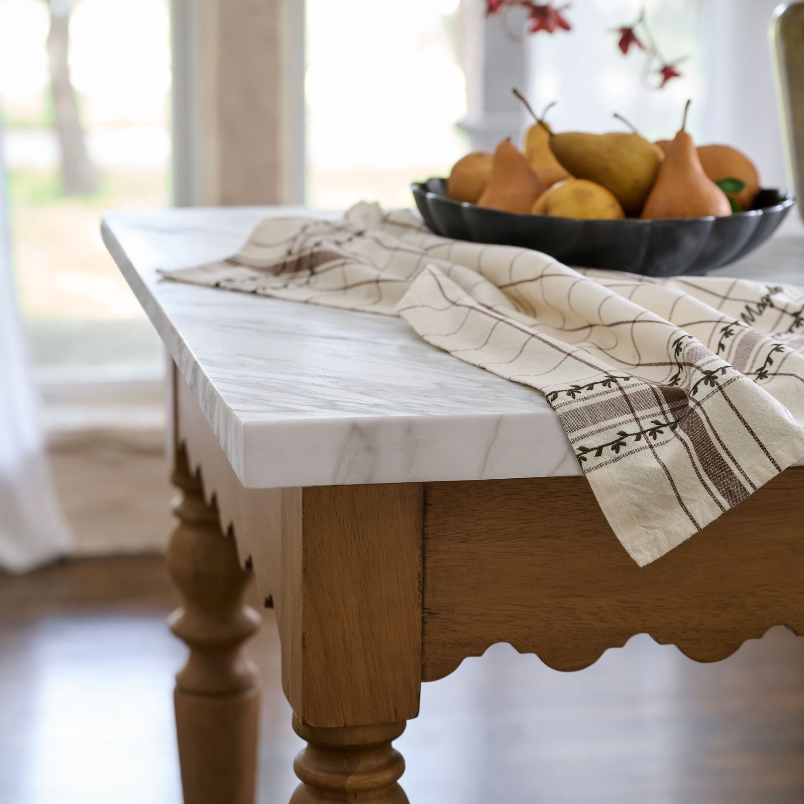 Wooden table with marble top and bowl of pears in a bright room