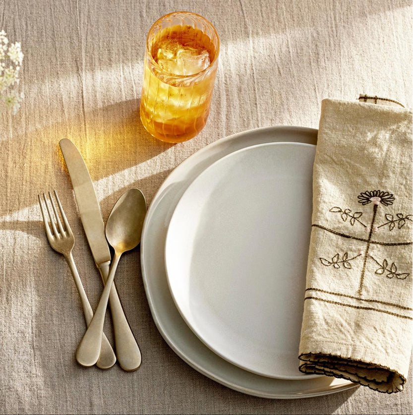 Set table with white plates, silverware, and a glass of orange juice on a textured surface.