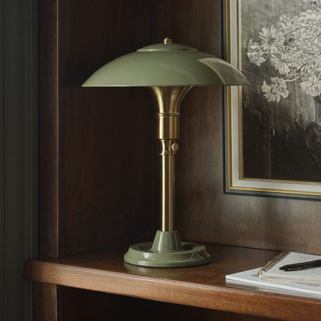Green table lamp on a wooden surface with a painting in the background