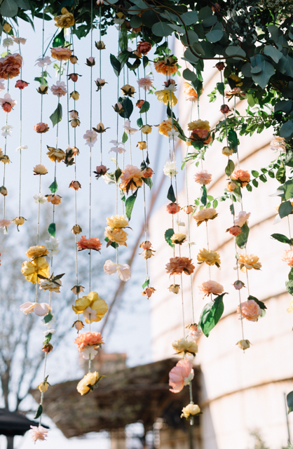 Decorative floral arch with hanging flowers and greenery against a blurred outdoor background.