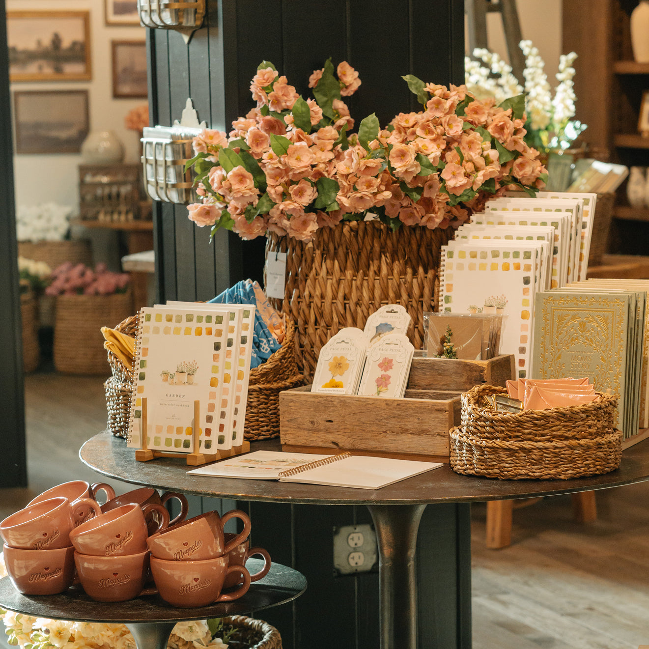 Table with decorative items including flowers, baskets, and mugs in Magnolia Market.