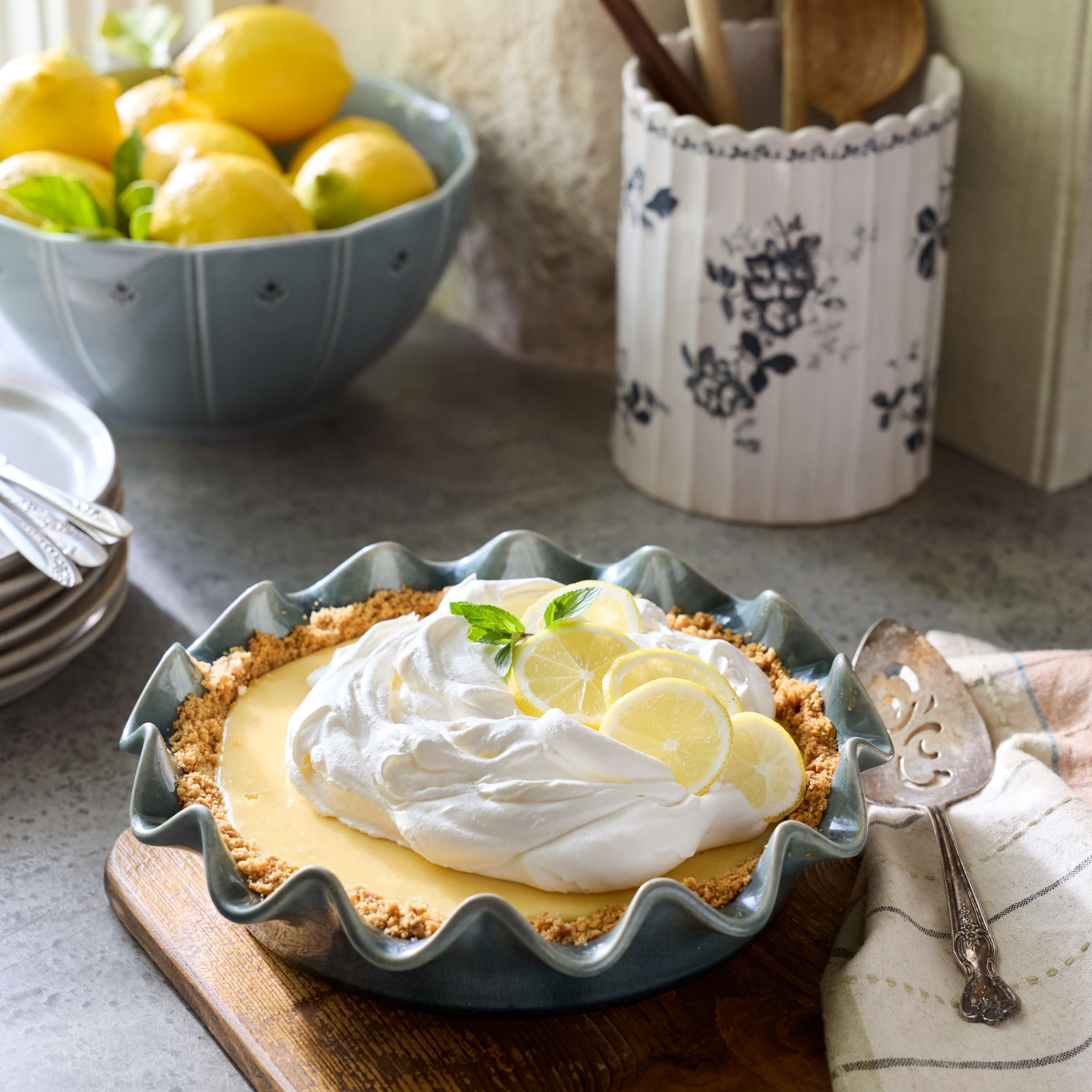 Lemon pie with whipped cream on a wooden cutting board with lemons in the background.