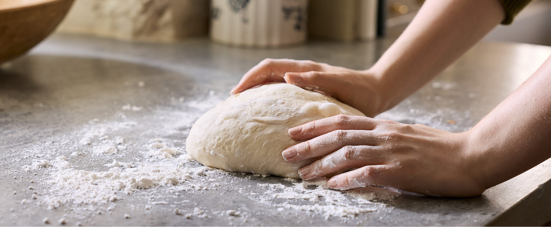 two hands kneading sourdough on a cement surface.