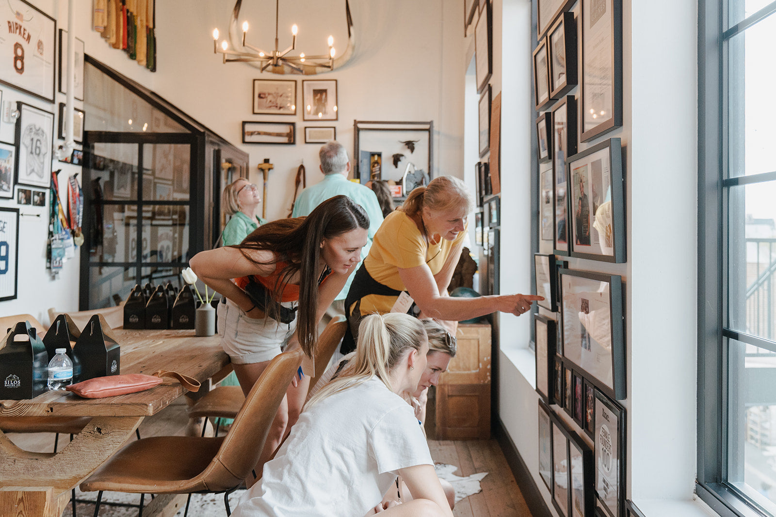 People looking at framed pictures on a wall in Chip Gaines office with a window and furniture.