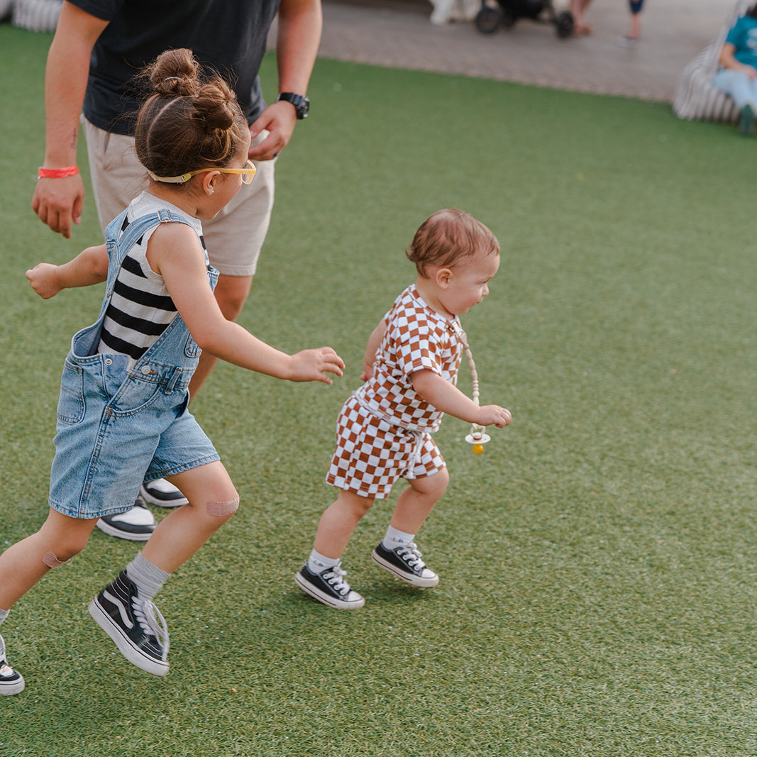 Two children running on a grassy field with an adult nearby.