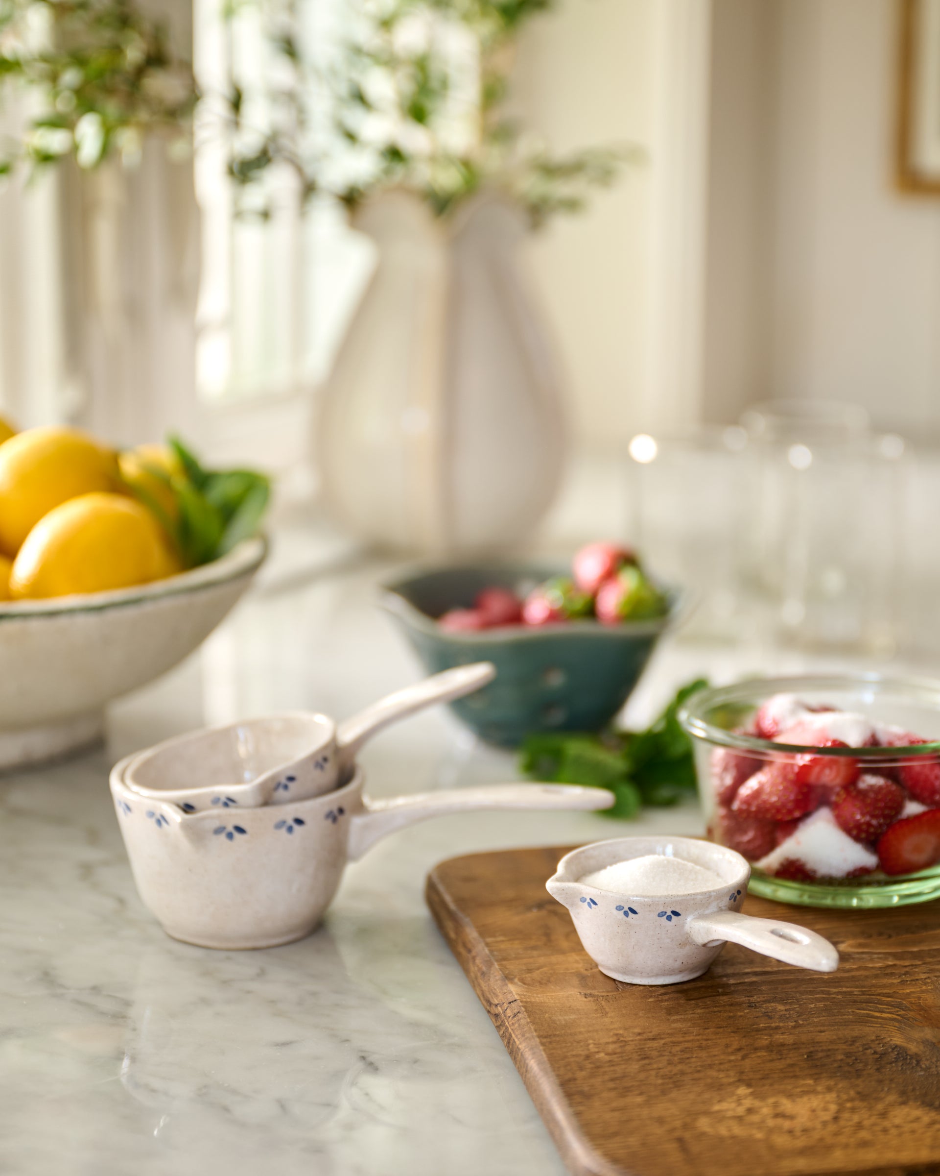Kitchen counter with measuring cups, lemons, and strawberries on a marble surface.