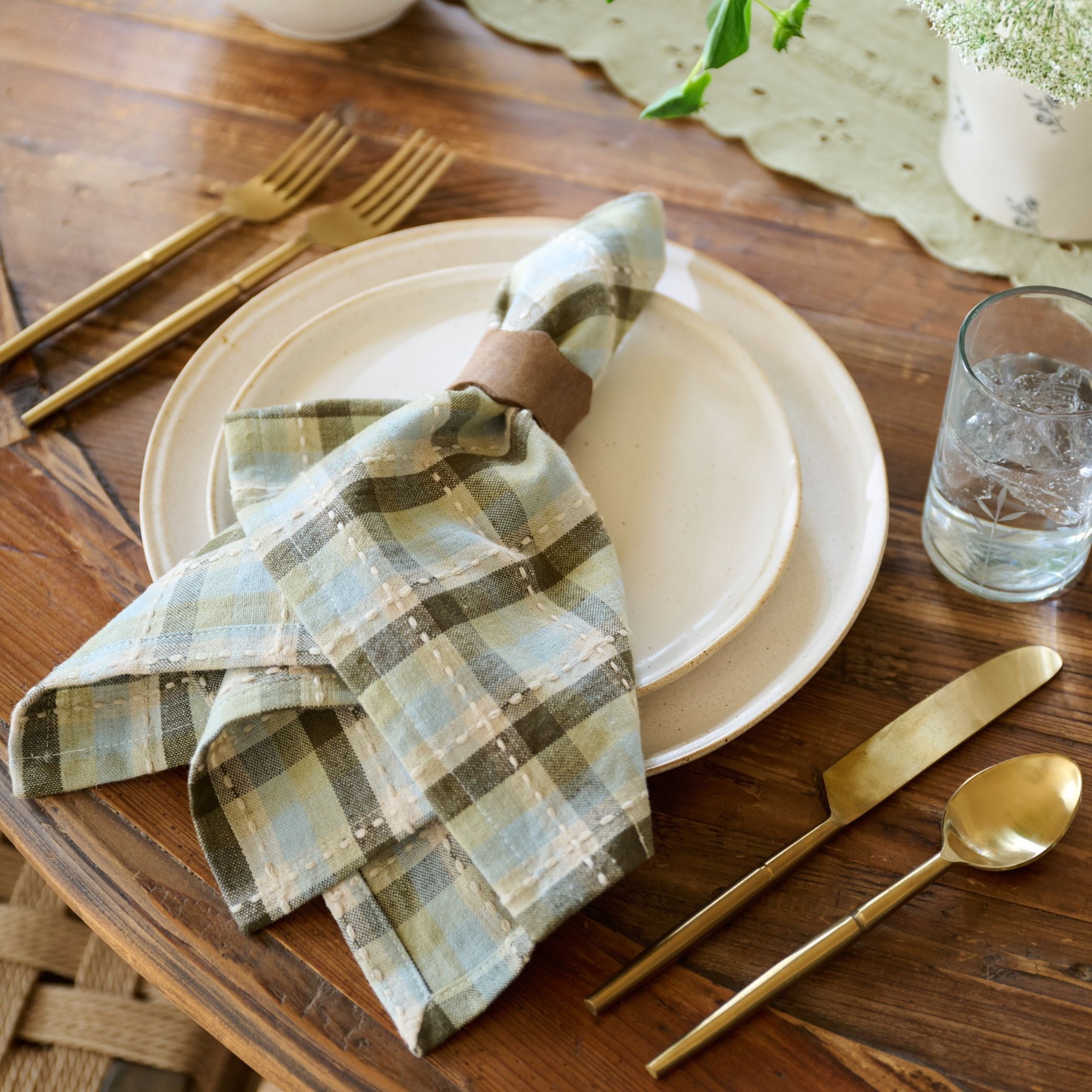 folded napkin on a dinner plate with gold flatware on a wooden table top.