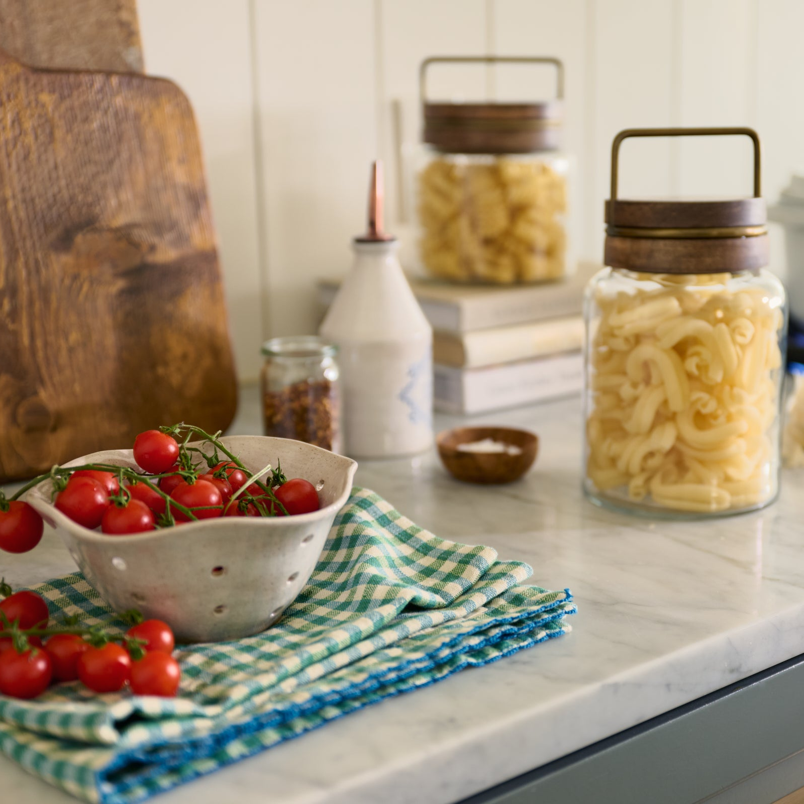 Kitchen counter with tomatoes, pasta, and jars on a checkered towel