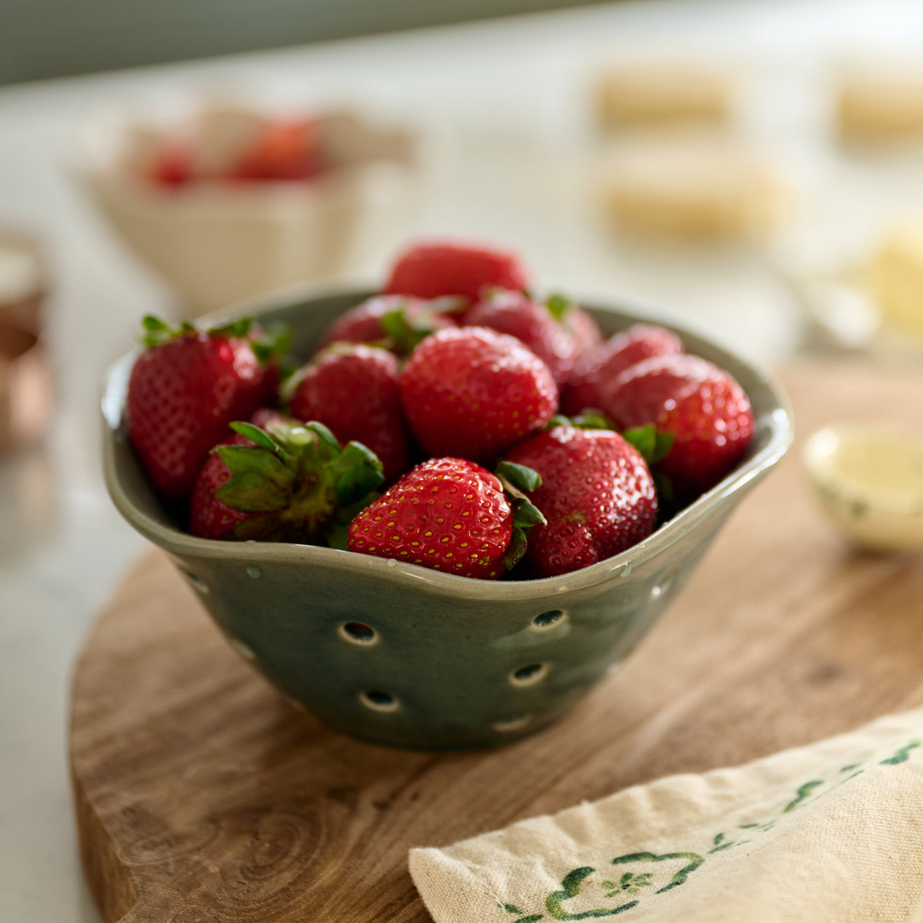 Green colander filled with strawberries on a wooden surface