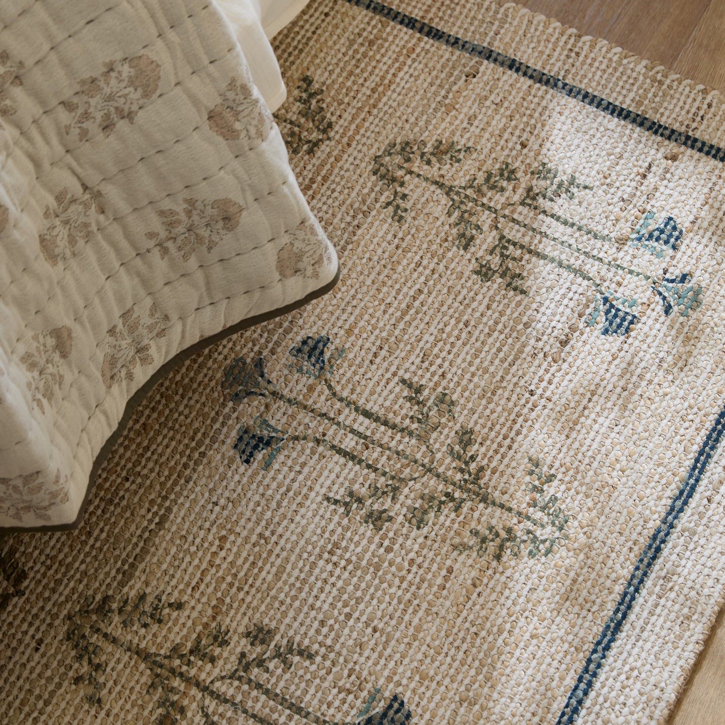 Sylvie chive blue rug shown displayed under a bed draped with neutral bedding