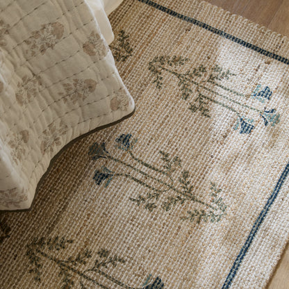 Sylvie chive blue rug shown displayed under a bed draped with neutral bedding