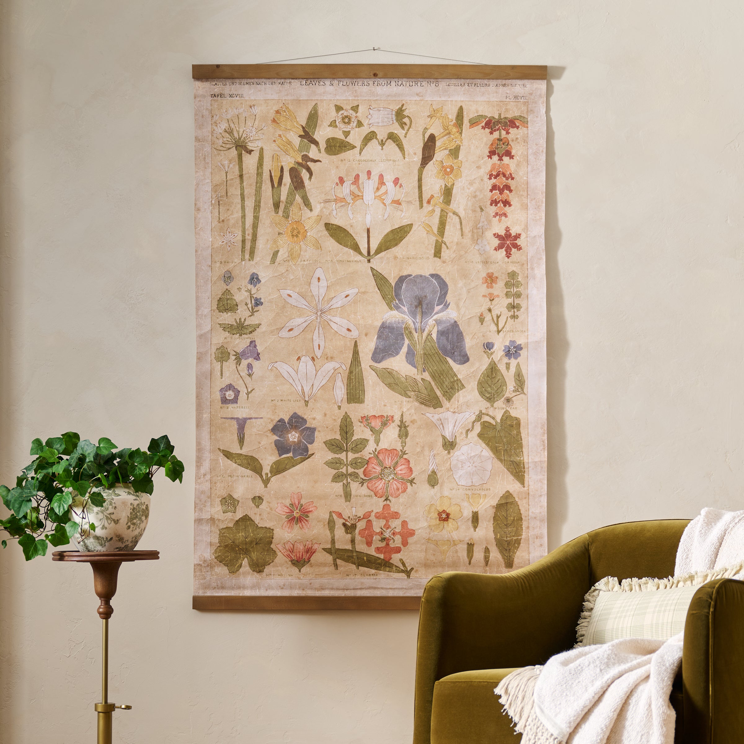 Floral tapestry hanging on a wall above a green armchair with a plant beside it.