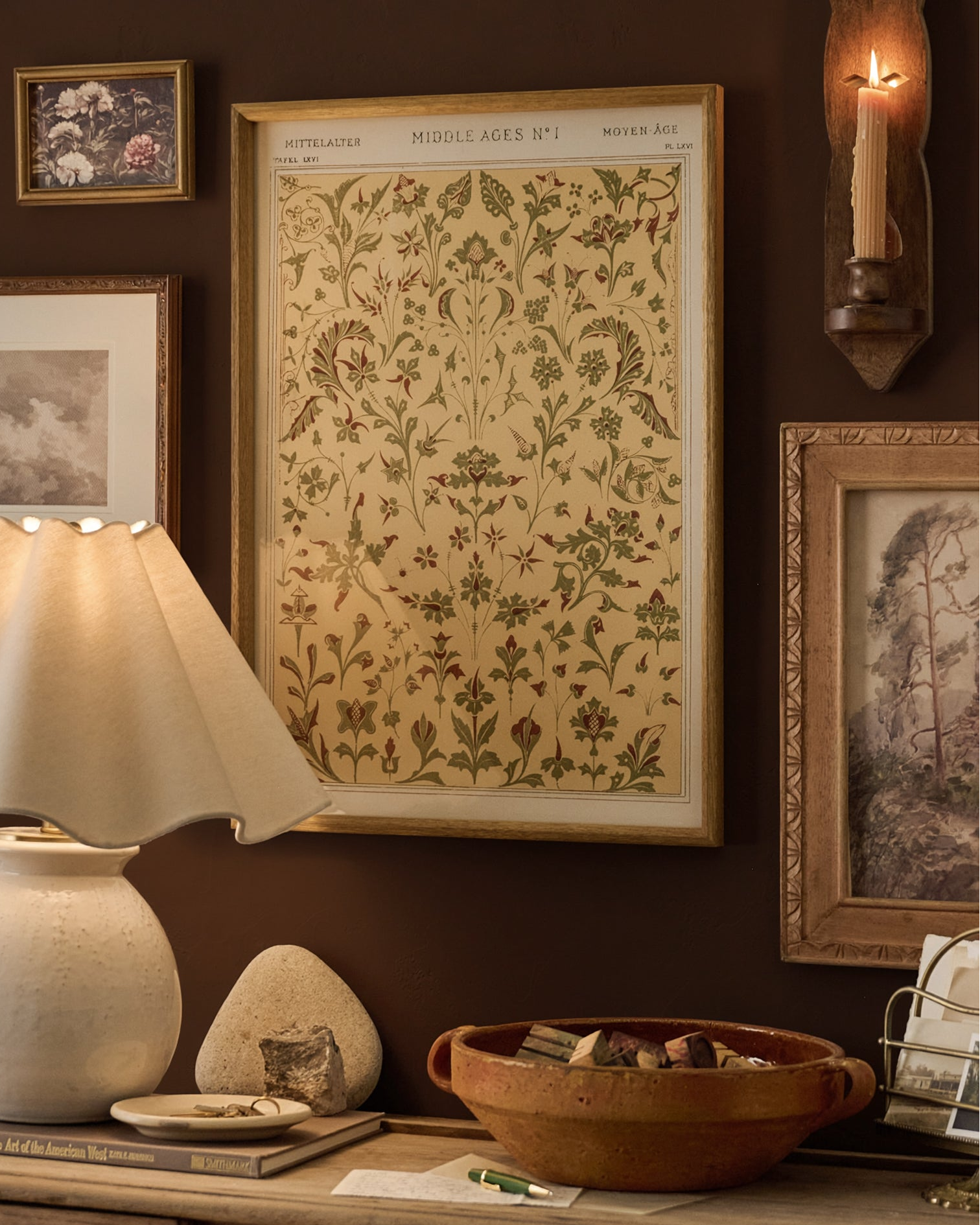 A framed vintage botanical print titled 'MIDDLE-AGES NO. 1' hangs on a dark brown wall in a styled room setting with a lamp, ceramic bowl, and other framed art.