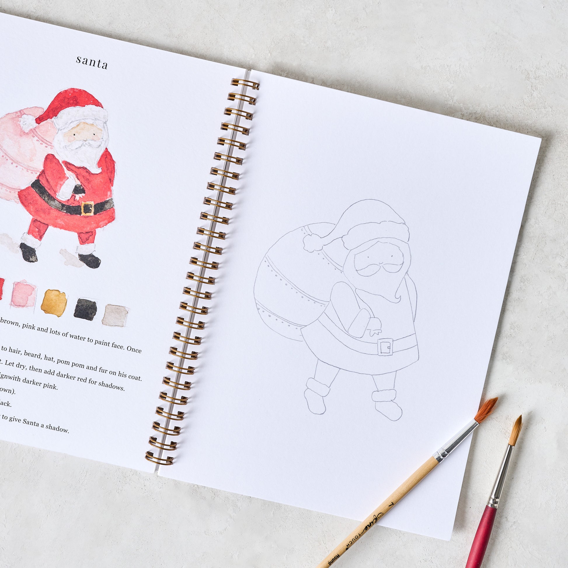 Christmas Watercolor Workbook shown open with paintbrushes