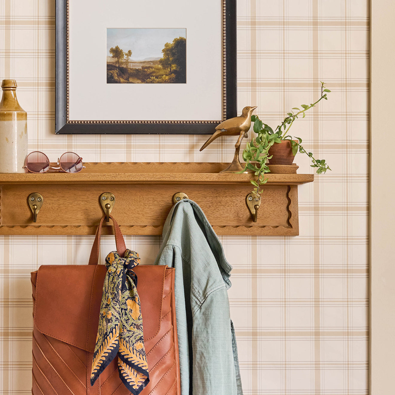 Wooden shelf with hooks holding a brown leather bag, light blue jacket, and decorative items against a plaid wall.