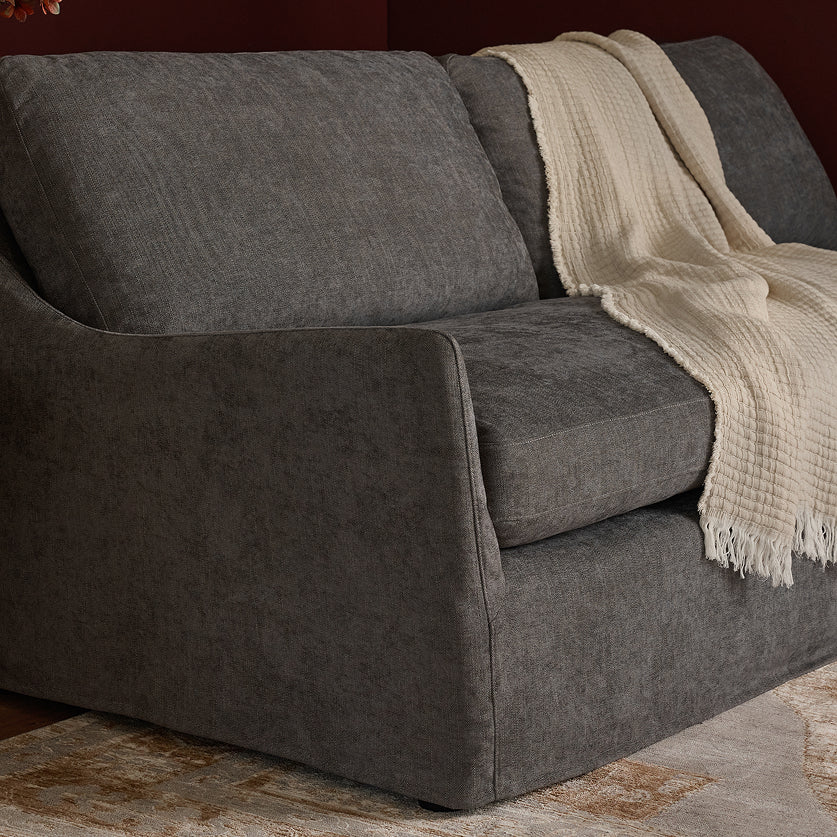 A dark gray upholstered loveseat or recliner chair shown in a styled interior setting, with a cream throw blanket draped over the seat and back.