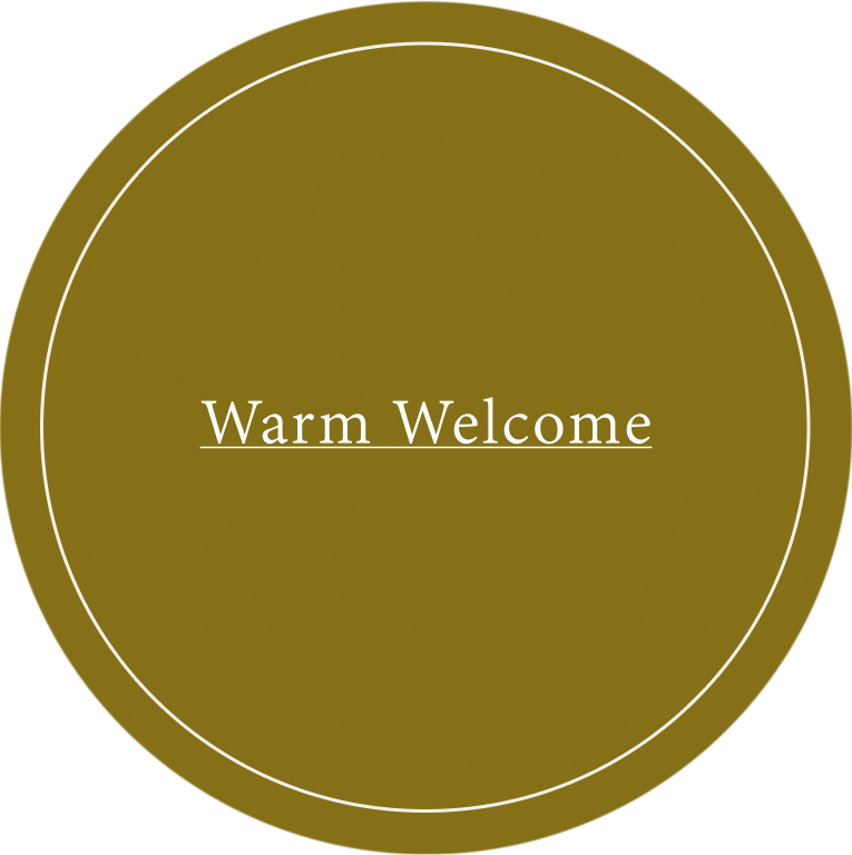 A circular olive green sign with a thin white inner circle and the words 'Warm Welcome' in white serif text at the center, shown on a white background.